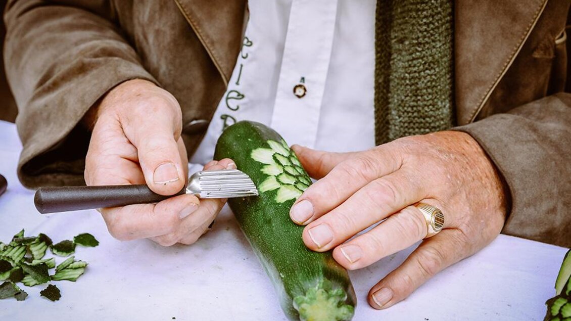 Eine Person schnitzt mit einem speziellen Werkzeug ein Muster in eine Zucchini. Grünes Gemüse wird kreativ bearbeitet. | © Foto Freisinger