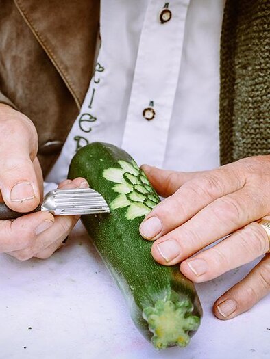 A person is carving a pattern into a zucchini with a special tool. Green vegetables are being creatively processed. | © Foto Freisinger