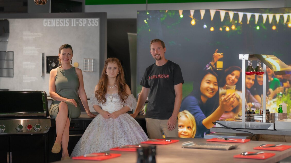 Eine Gruppe von drei Personen steht in einer modernen Küche. Im Hintergrund sind festliche Lichter und ein Familienfoto zu sehen. | © Bernd Widmoser