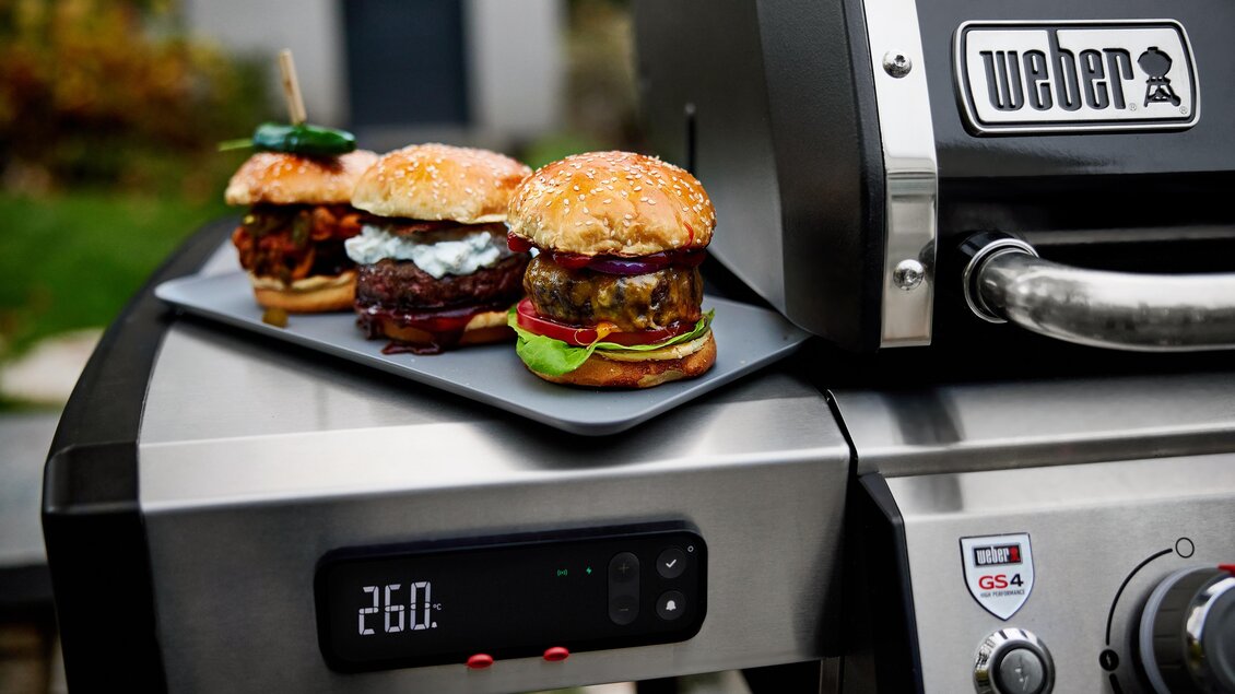 Drei leckere Hamburger auf einem Grill. Der Grill zeigt eine Temperatur von 26 Grad. | © Weber Grill