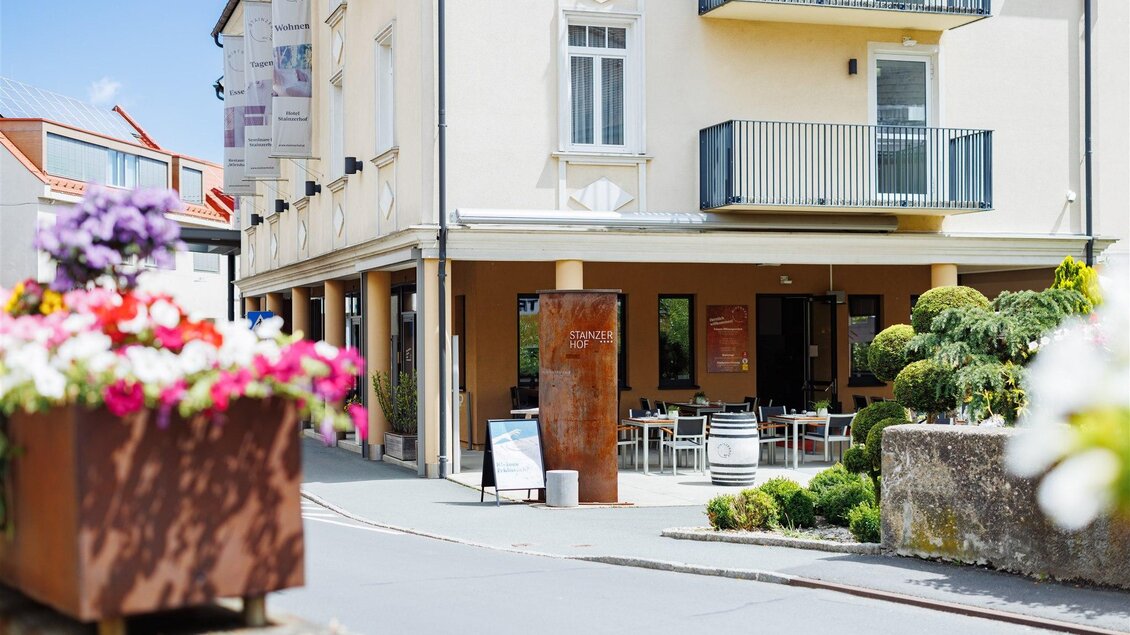 Ein gemütliches Restaurant mit Sitzplätzen im Freien und einer blühenden Pflanzenterrasse. Die Fassade ist hell und einladend, umgeben von einer schönen Umgebung. | © Stainzerhof - Kathrin Messner