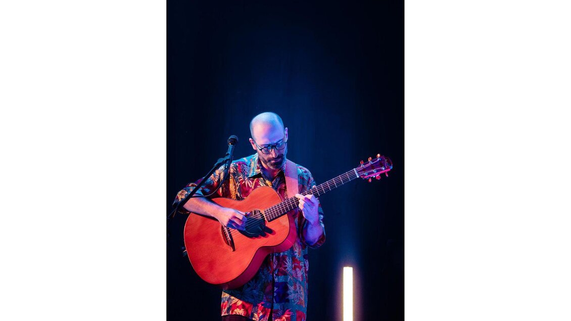 Ein Bild des Gitarristen und Sängers Georg Neureiter in einem dunklen Raum mit Neonlichtern im Hintergrund und einer Gitarre in der Hand. | © Kevin Hubeling