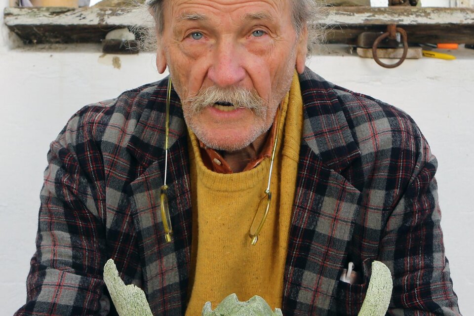 Ein älterer Mann sitzt mit einem grünen Kunstwerk in seinen Händen. Er trägt eine traditionelle Mütze und hat ein freundliches Lächeln. | © Gerald Brettschuh Foto_Pachernegg 01