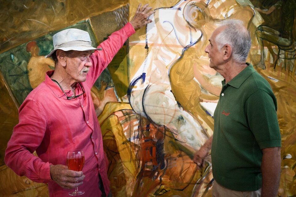 Zwei Männer unterhalten sich lebhaft vor einem Gemälde. Der Mann links trägt ein rotes Hemd und hält ein Glas in der Hand, während der andere in einem grünen Polo stark interessiert wirkt. | © Ulrike Rauch
