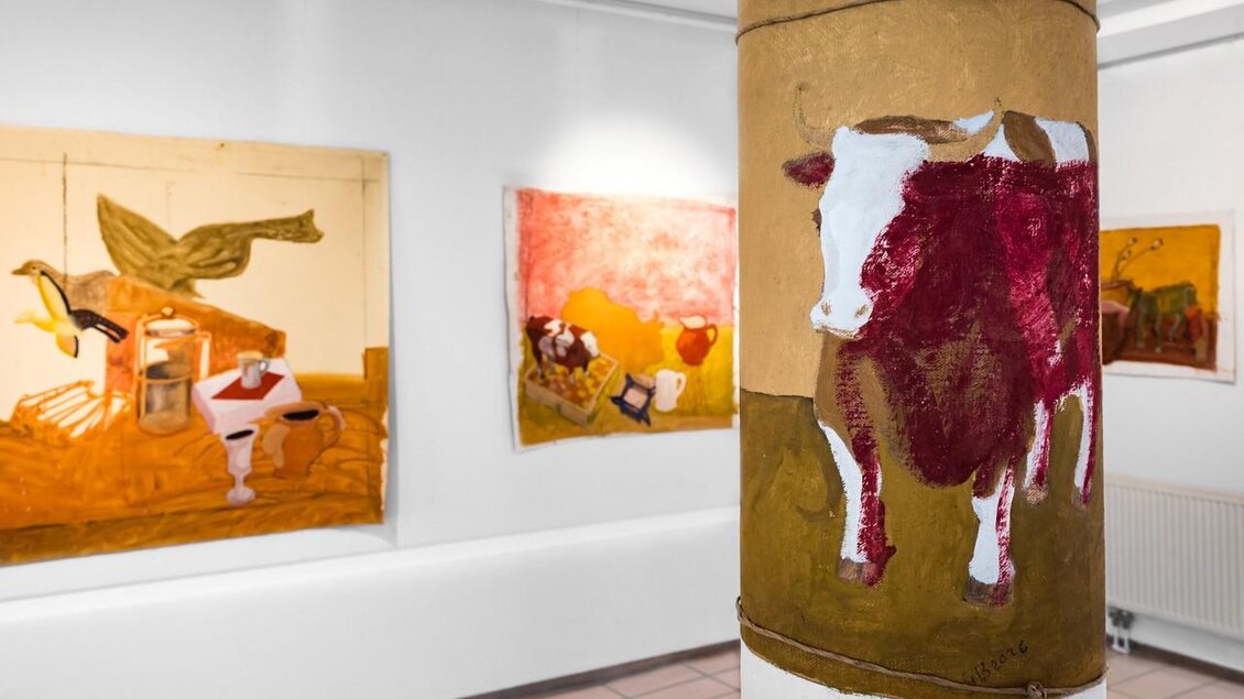 Eine Galerie mit bunten Gemälden, die Tiermotive zeigen. Im Vordergrund ist eine bemalte Säule mit einem roten und weißen Kuhmotiv. | © Ulrike Rauch