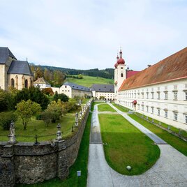 Ein historisches Klostergebäude mit roten Dächern und einer umgebenen grünen Landschaft. Die Anlage ist von Bäumen und einem gepflegten Weg umgeben. | © Tv Murau