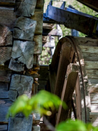 A wooden wheel near an old waterwheel. Surrounded by green leaves and sunny light. | © Holzmuseum
