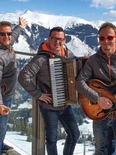 Eine Gruppe von fünf Männern in sportlichen Jacken steht in den Bergen. Sie spielen Instrumente und genießen die sonnige Winterlandschaft. | © Riesneralm