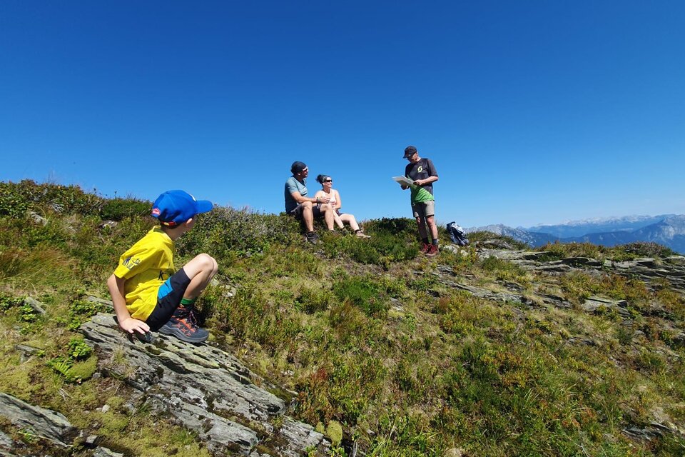 Eine Gruppe von Personen sitzt auf einem Berg mit einer schönen Aussicht. Ein Kind erkundet die Umgebung auf dem Felsen. | © Hubert Pleninger