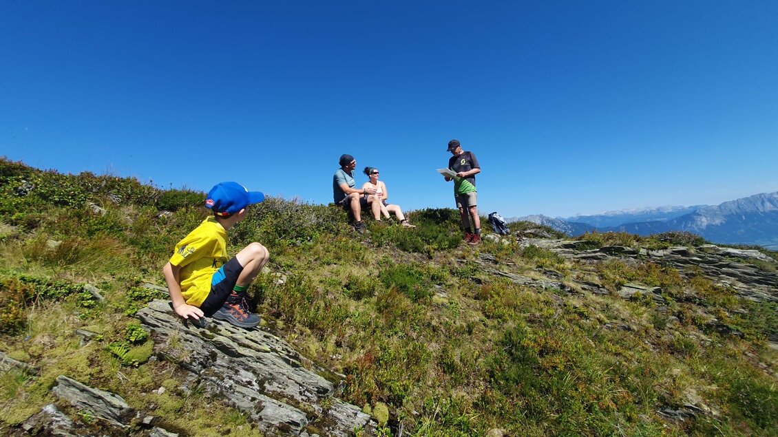 Eine Gruppe von Personen sitzt auf einem Berg mit einer schönen Aussicht. Ein Kind erkundet die Umgebung auf dem Felsen. | © Hubert Pleninger