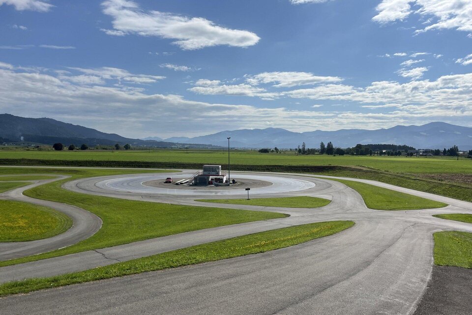 Ein Testgelände mit verschiedenen Fahrbahnkurven und einer großen, offenen Landschaft im Hintergrund. Der Himmel ist teilweise bewölkt und es sind Berge in der Ferne sichtbar. | © Peter Hopf