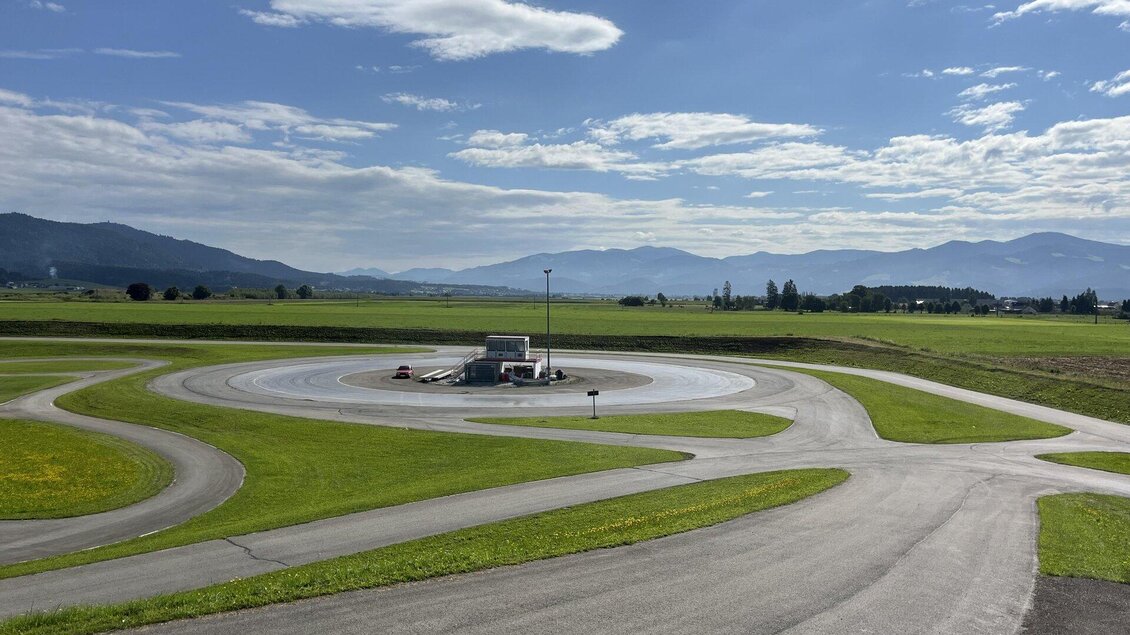 Ein Testgelände mit verschiedenen Fahrbahnkurven und einer großen, offenen Landschaft im Hintergrund. Der Himmel ist teilweise bewölkt und es sind Berge in der Ferne sichtbar. | © Peter Hopf