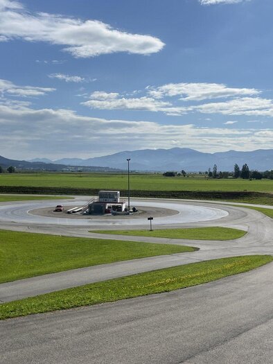 A test site with various road curves and a large open landscape in the background. The sky is partially cloudy and mountains are visible in the distance. | © Peter Hopf