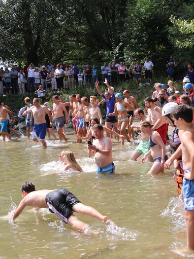Eine Gruppe von Kindern und Jugendlichen steht im Wasser und spielt. Zuschauer beobachten das Geschehen am Ufer. | © GlaMur
