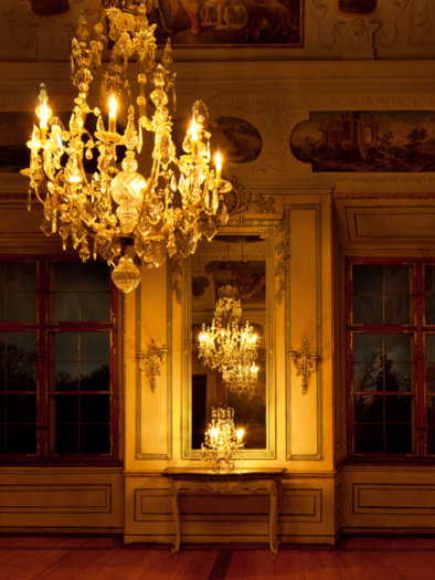 An elegant room with a magnificent chandelier and large windows. The walls are decorated with intricate paintings.