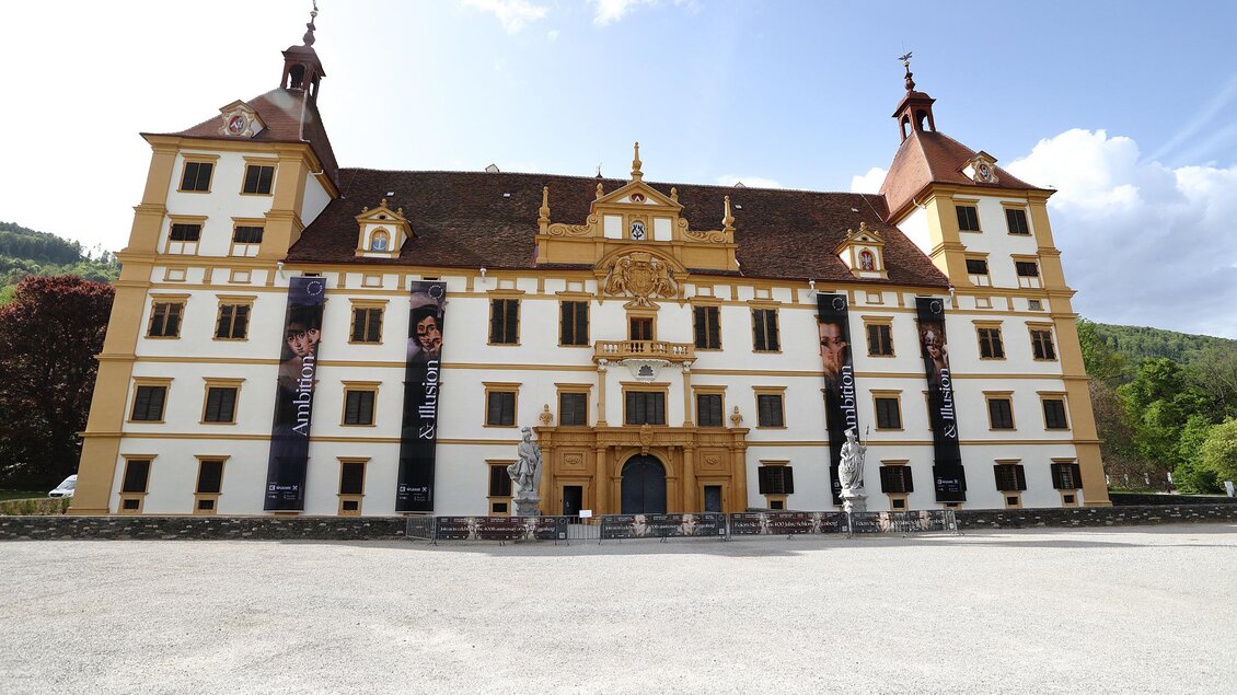 Ein beeindruckendes Schloss mit einer auffälligen Fassade und zwei markanten Türmen. Das Gebäude ist von einem großen Platz umgeben und präsentiert sich inmitten einer malerischen Landschaft. | © (c)Universalmuseum JoanneumJ.J. Kucek.