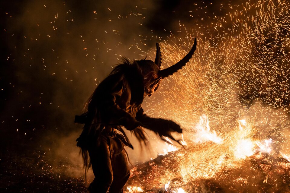 Eine dunkle Szene mit einem gefleckten Wesen in einem Kostüm mit Hörnern. Funken sprühen aus einem Feuer im Hintergrund. | © Adobe Stock