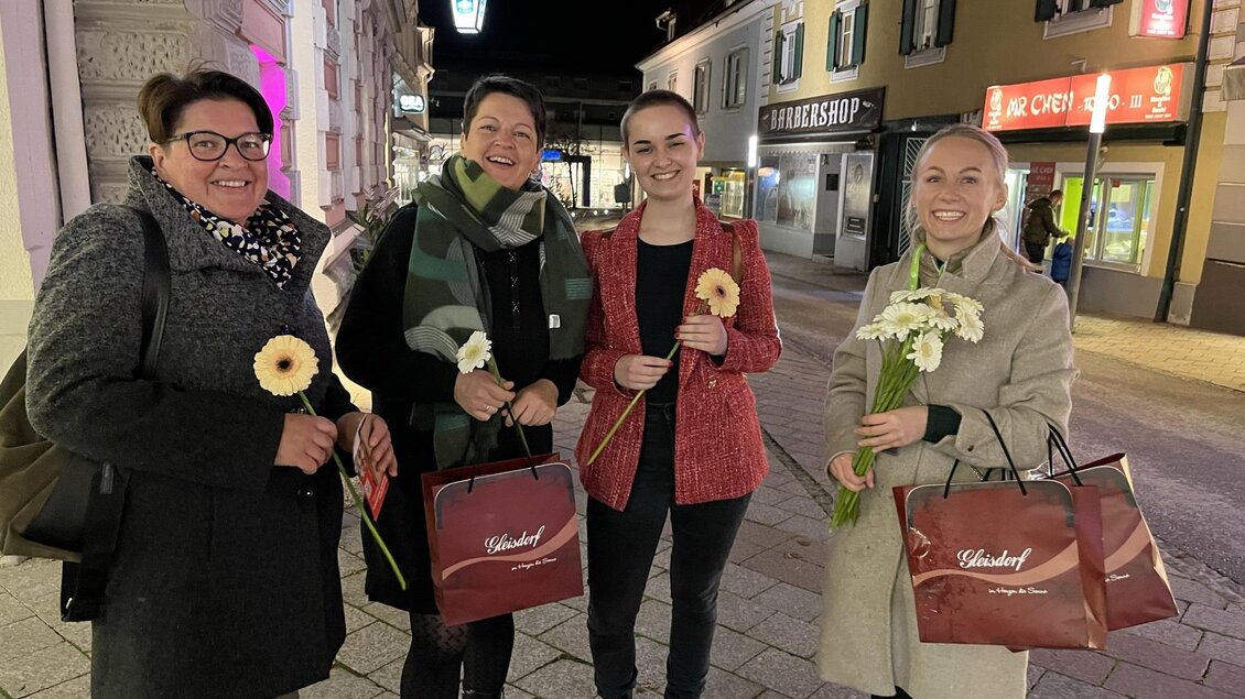 Vier Frauen stehen lächelnd auf einer Straße bei Nacht. Sie halten Blumen und Tüten in den Händen. | © Tourismusverband Oststeiermark