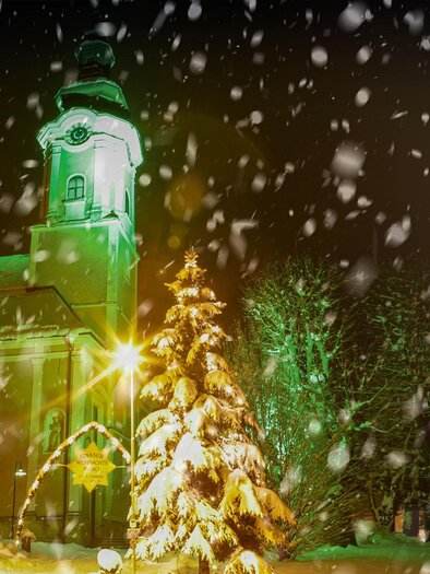 A church in the snow with festively lit fir trees. Snowflakes are gently falling in the dark. | © Johannes Platzer