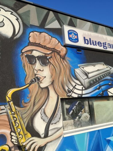 A colorful mural featuring a woman playing the saxophone. In the background, musical elements and the logo of a company are visible. | © TVB_Steininger