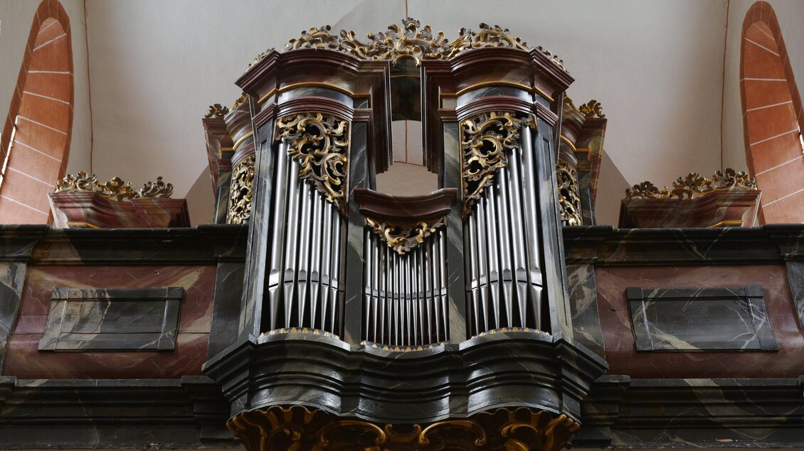 Eine prächtige Kirchenorgel aus Holz mit detaillierten Verzierungen. Die Orgel steht an der Wand und ist ein zentraler Blickfang im Raum.