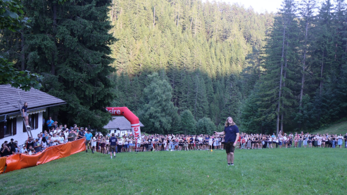 Ein großes Publikum versammelt sich auf einer Wiese, um ein Event zu beobachten. Im Hintergrund sind Bäume und eine Berghütte sichtbar. | © LJ Langenwang