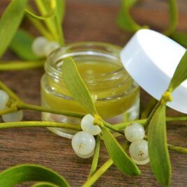 Ein Glastiegel mit grünem Balsam steht zwischen Mistelzweigen. Die frischen, weißen Beeren und grünen Blätter verleihen dem Bild eine natürliche Note. | © Martina Schmidt