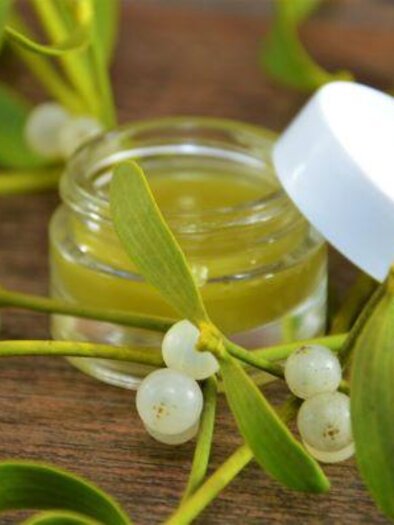 Ein Glastiegel mit grünem Balsam steht zwischen Mistelzweigen. Die frischen, weißen Beeren und grünen Blätter verleihen dem Bild eine natürliche Note. | © Martina Schmidt