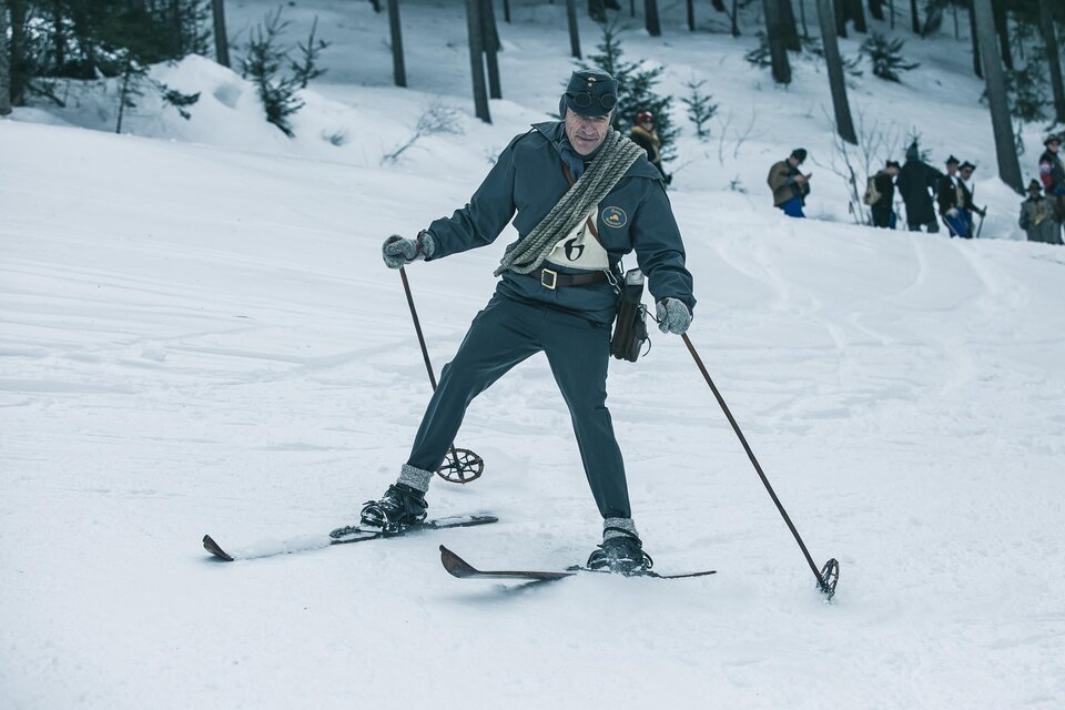 Ein Skifahrer in einer historischen Uniform fährt durch den Schnee. Im Hintergrund sind Menschen sichtbar, die zuschauen. | © Oliver Königshofer