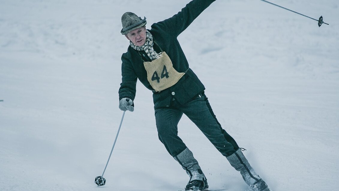 Ein älterer Mann fährt Ski in der verschneiten Landschaft. Er trägt einen traditionellen Anzug und hat eine Startnummer auf dem Rücken. | © Oliver Königshofer
