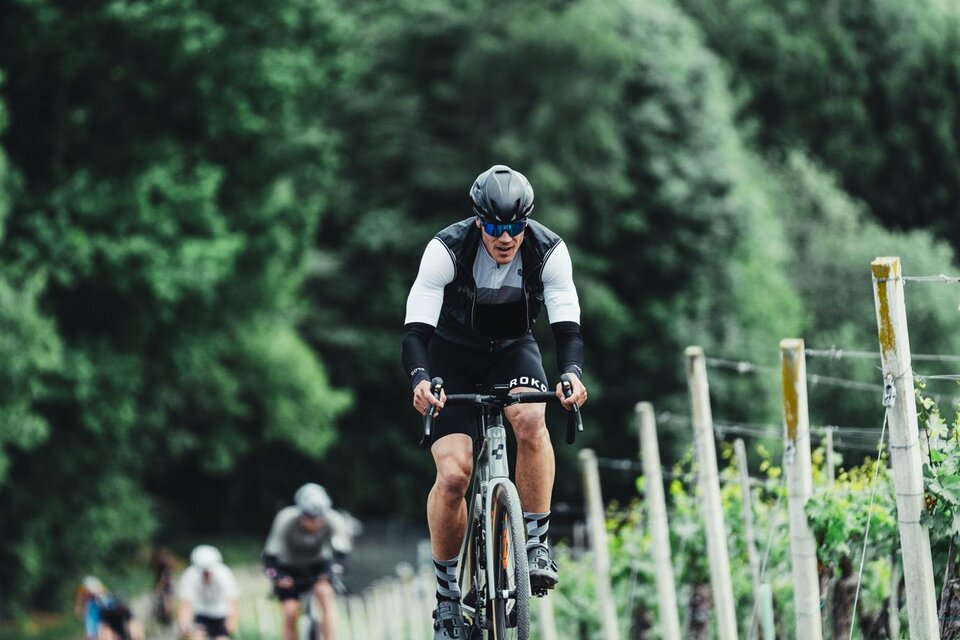 Ein Radfahrer fährt einen mit Kies bedeckten Weg bergauf, umgeben von Weinreben. Im Hintergrund sind grüne Hügel und Bäume sichtbar. | © hofstaetter@finisher-magazin.at