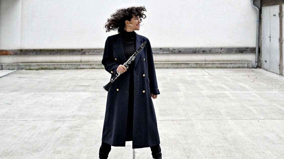 Klarinettistin Mona Matbou Riahi steht mit Instrument im Freien und blickt zur Seite bei Schlossträume des Storytelling Festivals. | © Nina Streets