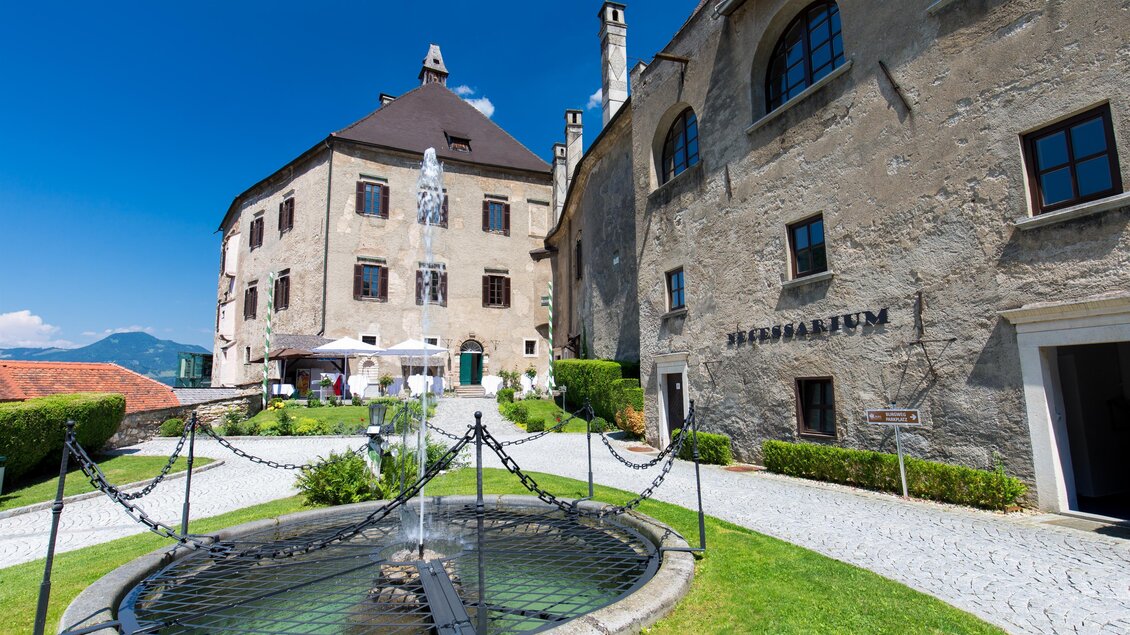 Innenhof von Burg Rabenstein mit Springbrunnen, Rasenfläche und gepflasterten Wegen, die Fassade ist Steingrau mit Blick zum Hauptgebäude in Frohnleiten. | © Region Graz-Harry Schiffer