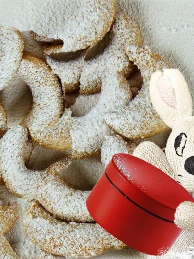 Eine bunte Figur mit einem Hasen und einer roten Schachtel steht neben Gebäck, das mit Puderzucker bestäubt ist. Im Hintergrund sind eingerollte Plätzchen zu sehen. | © Grazer Kasperltheater