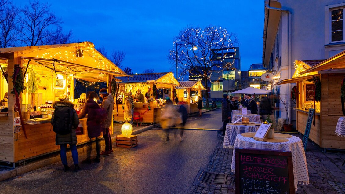 Ein festlicher Weihnachtsmarkt mit beleuchteten Ständen und Besuchern. Die Atmosphäre ist gemütlich und es ist bereits dunkel. | © Graz Tourismus - Harry Schiffer