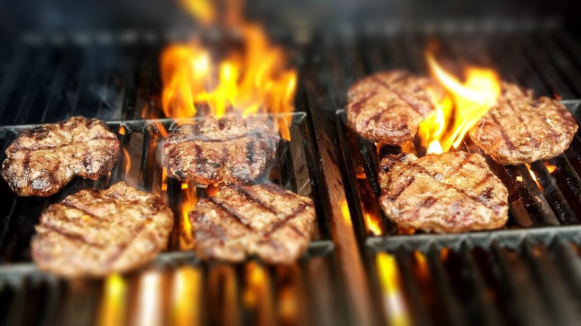 Leckere Burgerbratlinge grillen über offenem Feuer. Die Flammen sorgen für eine perfekte Grillfarbe und ein rauchiges Aroma.