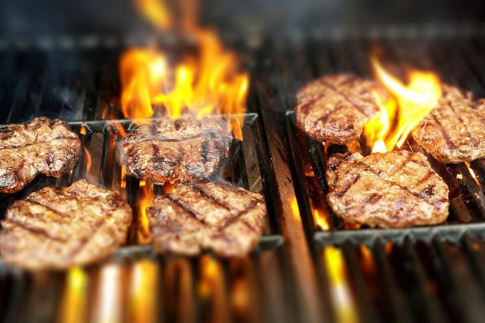 Leckere Burgerbratlinge grillen über offenem Feuer. Die Flammen sorgen für eine perfekte Grillfarbe und ein rauchiges Aroma.