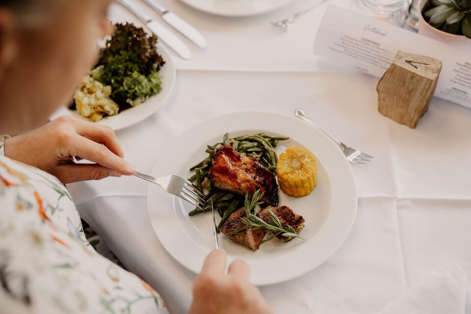 Ein Teller mit köstlichem Essen, darunter Fleisch, grüne Bohnen und Mais. Auf dem Tisch sind auch frischer Salat und Besteck zu sehen. | © LGH Wratschko