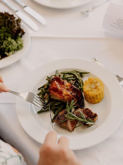 A plate with delicious food, including meat, green beans, and corn. There is also fresh salad and cutlery visible on the table. | © LGH Wratschko
