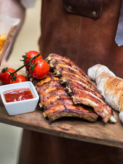 Egy fapadló grillezett bordákkal, friss paradicsommal, egy zsemlével és egy adag sült krumplival. Ehhez jár egy kis tál szósz. | © Painer Katrin