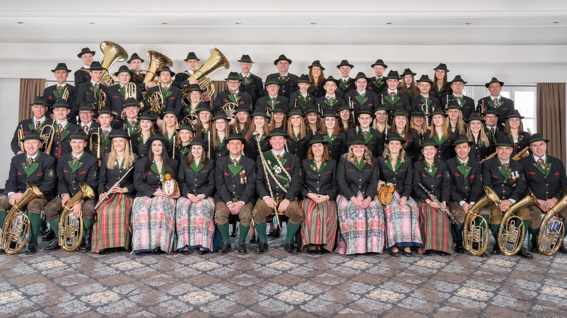 Eine große Musikgruppe steht in traditioneller Tracht. Sie halten verschiedene Musikinstrumente und schauen in die Kamera. | © MV Aigen im Ennstal