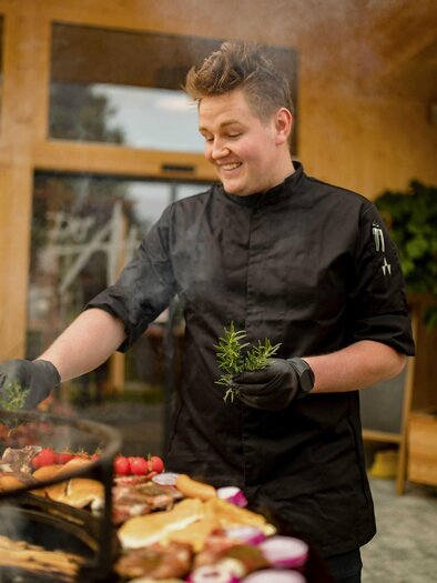 Zu sehen ist ein Koch beim Grillen mit Grillgut. | © Der Almblick