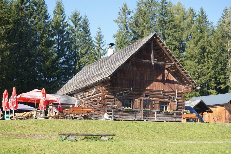 <p>Die Eselalm in Bad Mitterndorf mit einer Holzverkleidung und Sitzmöglichkeiten mit Sonnenschirmen im Freien ist umgeben von der grünen Landschaft des Ausseerlandes.</p> | © Eselalm, Bad Mitterndorf