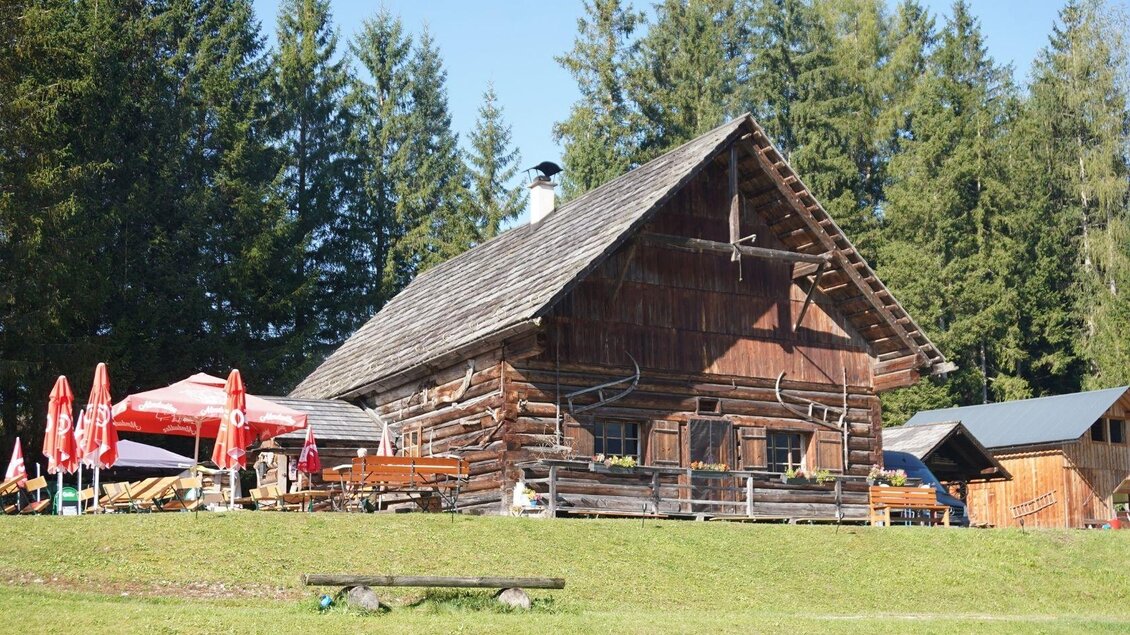 <p>Die Eselalm in Bad Mitterndorf mit einer Holzverkleidung und Sitzmöglichkeiten mit Sonnenschirmen im Freien ist umgeben von der grünen Landschaft des Ausseerlandes.</p> | © Eselalm, Bad Mitterndorf