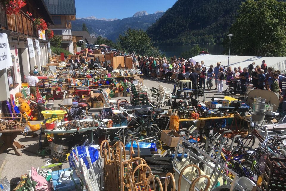 Ein Flohmarkt mit vielen verschiedenen Gegenständen und einer langen Schlange von Personen im Hintergrund. Die Umgebung ist von Bergen und einer schönen Landschaft umgeben. | © Freiwillige Feuerwehr Grundlsee