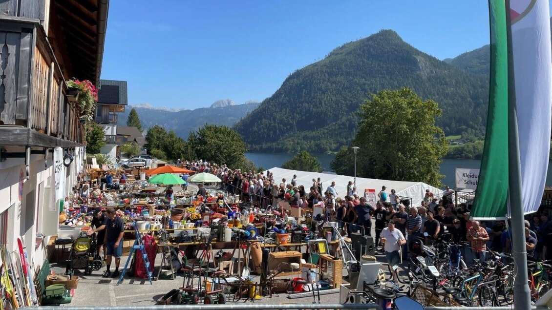 Ein Flohmarkt mit vielen Ständen, die verschiedene Waren anbieten. Im Hintergrund sind grüne Berge und ein klarer Himmel zu sehen. | © FF Grundlsee