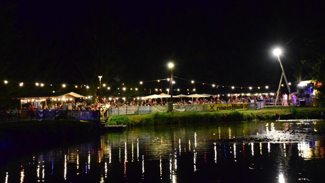 Eine lebhafte Nachtveranstaltung am Wasser mit festlicher Beleuchtung. Viele Menschen genießen die Atmosphäre unter den Lichtern. | © FF Altneudörfl