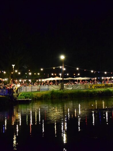 Eine lebhafte Nachtveranstaltung am Wasser mit festlicher Beleuchtung. Viele Menschen genießen die Atmosphäre unter den Lichtern. | © FF Altneudörfl