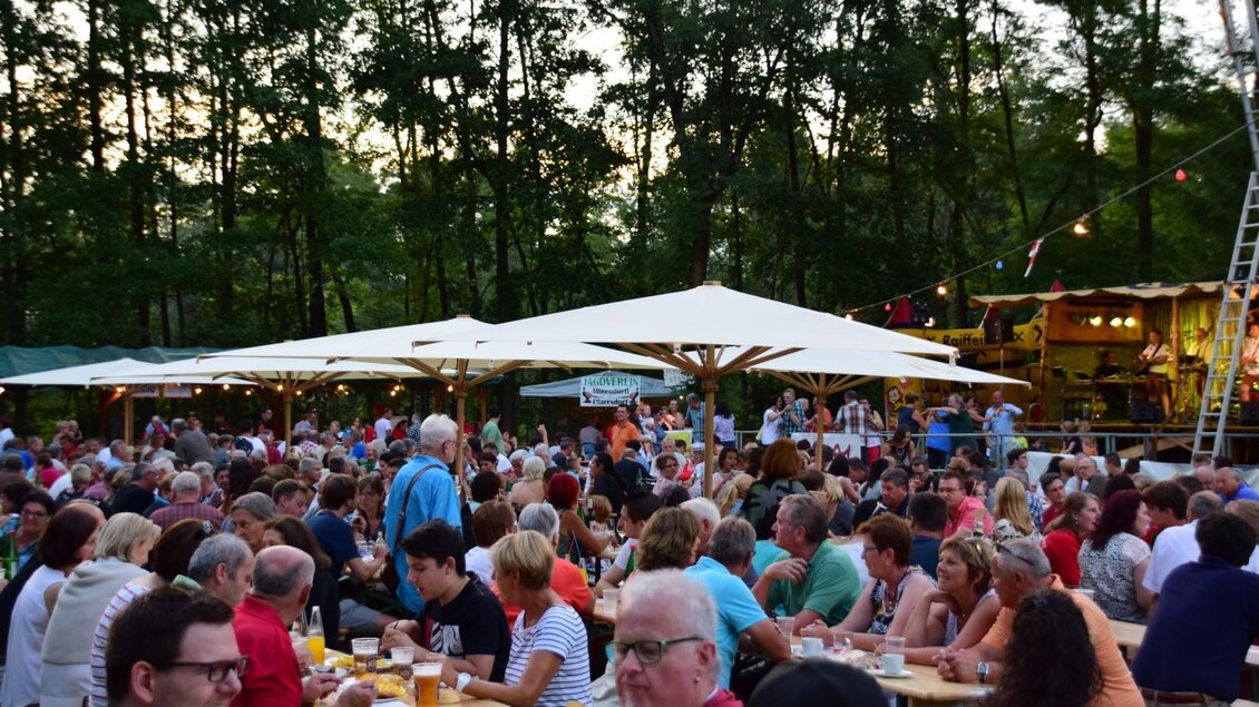 Ein belebtes Fest mit vielen Menschen unter Sonnenschirmen. Im Hintergrund sind Stände und Bäume sichtbar, alles in einer entspannten Abendatmosphäre. | © FF Altneudörfl