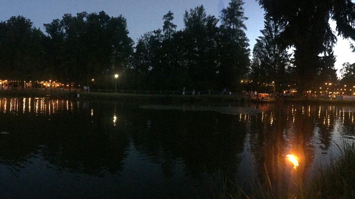 Ein ruhiger See bei Dämmerung, umgeben von Bäumen und Lichtern. Die Wasseroberfläche spiegelt die Lichter und die Umgebung wider. | © FF Altneudörfl